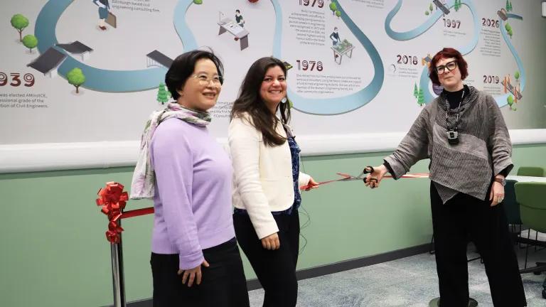 Professor Mao, Dr. Kirli and Dr. Highton cut the ribbon of The Molly Fergusson Room in front of a wall decal showing a timeline of Molly's achievements 