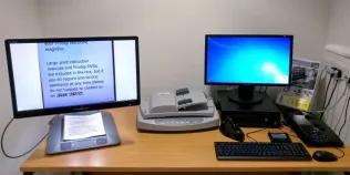 two accessible PCs sit on a desk with various assistive technology
