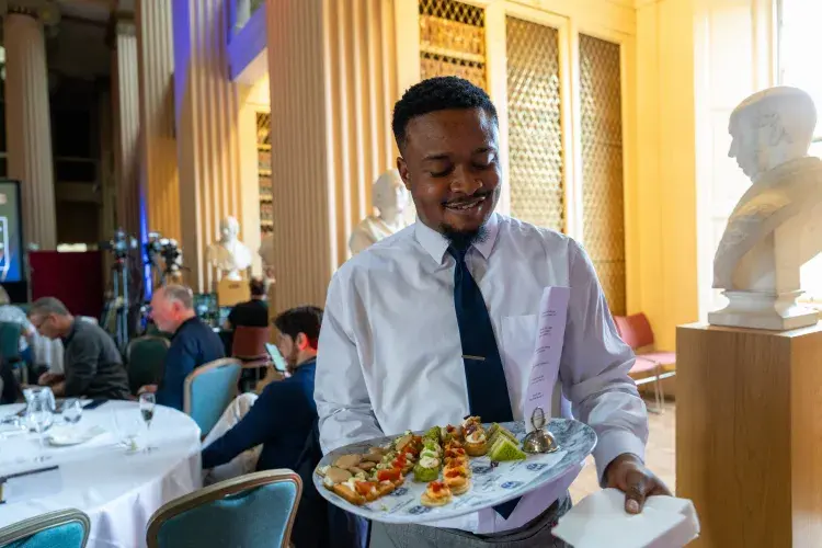 a member of catering staff smiling into the camera holding a tray of food