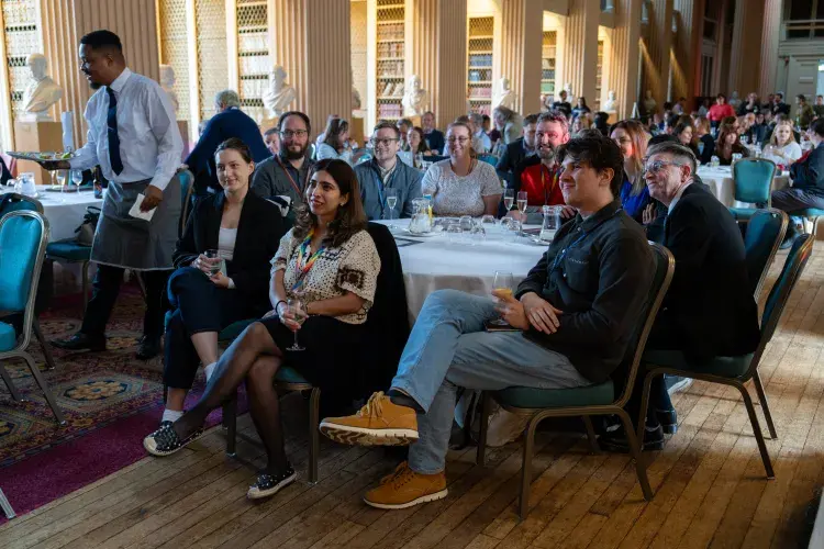 a wide shot of everyone in attendance sitting at tables looking to the front of the room 
