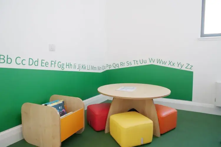 A low table with colourful soft cubes for children to sit on. The area is segmented from the rest of the room with green to indicate this is the space for children. 