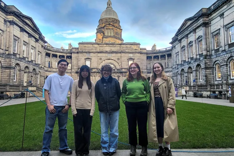 Five students standing in the Edinburgh Old College courtyard. Background: a lawn, encircling campus buildings, a tower