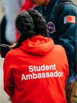 Photo of student wearing a red hoodie that says student ambassador on the back. 