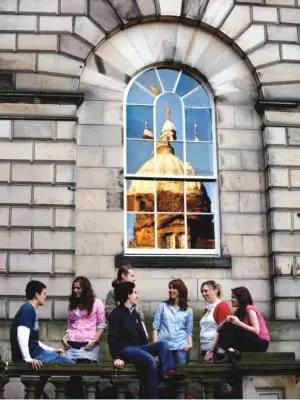A group of eight students underneath a window at Old College, with the window reflecting a bright yellow dome on another building.