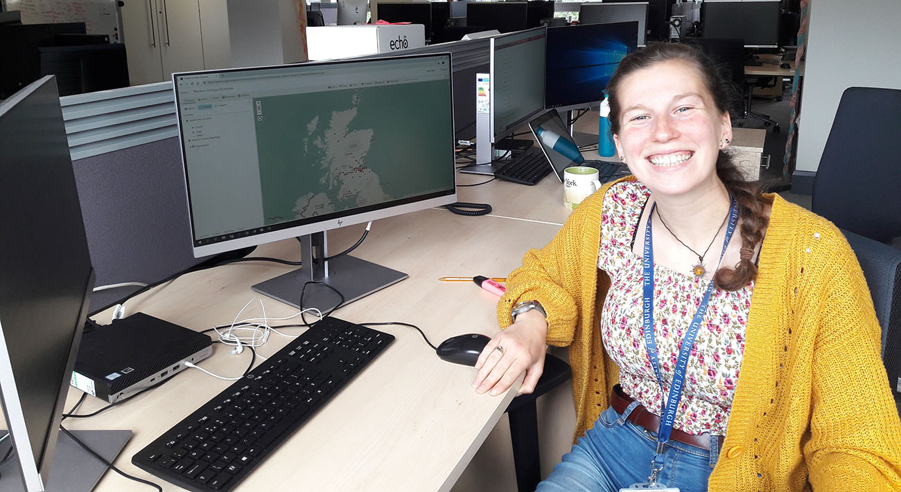 Emma Carroll sitting at her desk with witch visualisation on the computer display